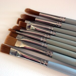 May include: A set of ten paint brushes with light blue handles and silver ferrules. The brushes have different sizes and shapes of bristles.