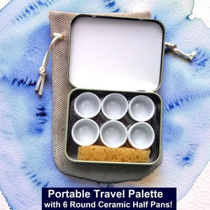 May include: A portable travel palette with six round ceramic half pans. The palette is in a metal tin, with a beige sponge and a beige drawstring bag. The background is a watercolor wash of blue and white.