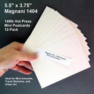 May include: A stack of off-white Magnani 1404 mini postcards, each measuring 5.5" x 3.75", held in a hand. The text on the image reads "140lb Hot Press Mini Postcards 12-Pack". A label reads "Magnani 1404 - 140lb Postcards Hot Press (Portofino)".