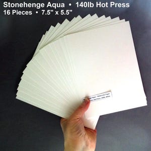 May include: A stack of 16 sheets of Stonehenge Aqua watercolor paper, hot press, 7.5" x 5.5", 140lb. The paper is held in a hand and fanned out. The text "Stonehenge Aqua" and other details are visible.
