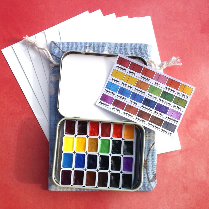 Puede incluir: Un juego de pintura de acuarela en una lata de metal, con una variedad de colores. Incluye una carta de colores y una peque&ntilde;a pila de papel blanco. La lata est&aacute; dentro de una bolsa de tela azul con cord&oacute;n.