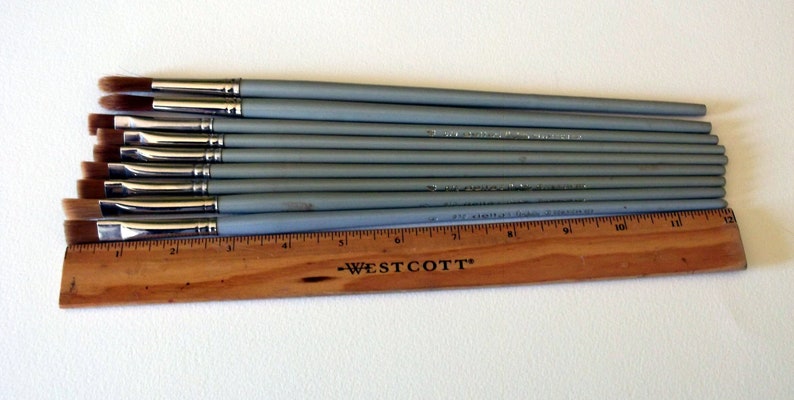 May include: A set of ten gray paint brushes with brown bristles, arranged in order of size, with a wooden ruler labeled "Westcott" underneath.