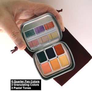 May include: A small, open metal watercolor paint set with six quarter pan colors, three granulating colors, and three pastel tones. The set is held over a maroon velvet pouch. The paint colors include green, blue, orange, and yellow. The text on the image reads: "6 Quarter Pan Colors, 3 Granulating Colors, 3 Pastel Tones."