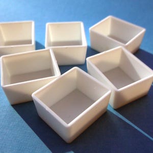 May include: Set of six white square watercolor paint pans. The pans are arranged in a circle with the opening facing up.
