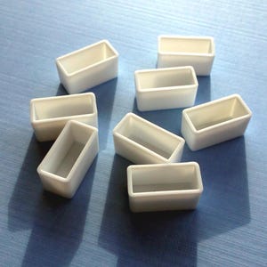 May include: Eight white rectangular plastic containers, possibly for paint or other small items, are arranged in a semi-circle on a blue surface.