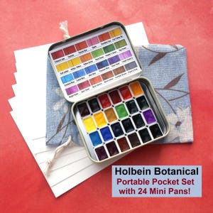 Puede incluir: Un juego de acuarelas de bolsillo port&aacute;til Holbein Botanical con 24 mini godets. La lata abierta presenta una variedad de colores vibrantes. El juego se muestra sobre una tela azul con estampado floral y papel blanco.