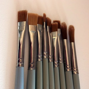 May include: A set of ten paint brushes with silver metal ferrules and light blue wooden handles. The brushes have various sizes and shapes of bristles.