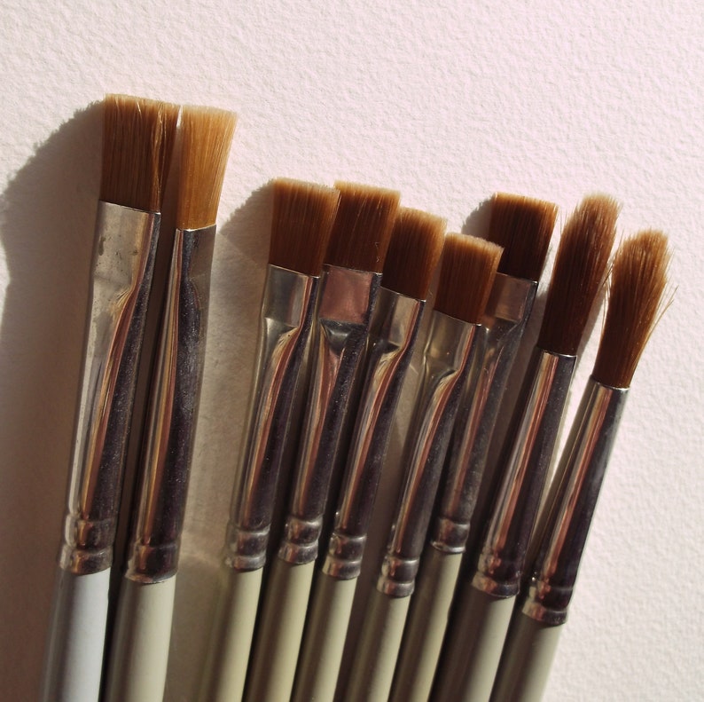 May include: A set of nine paint brushes with brown bristles and silver handles. The brushes are arranged in a row, with the largest brush on the left and the smallest brush on the right.