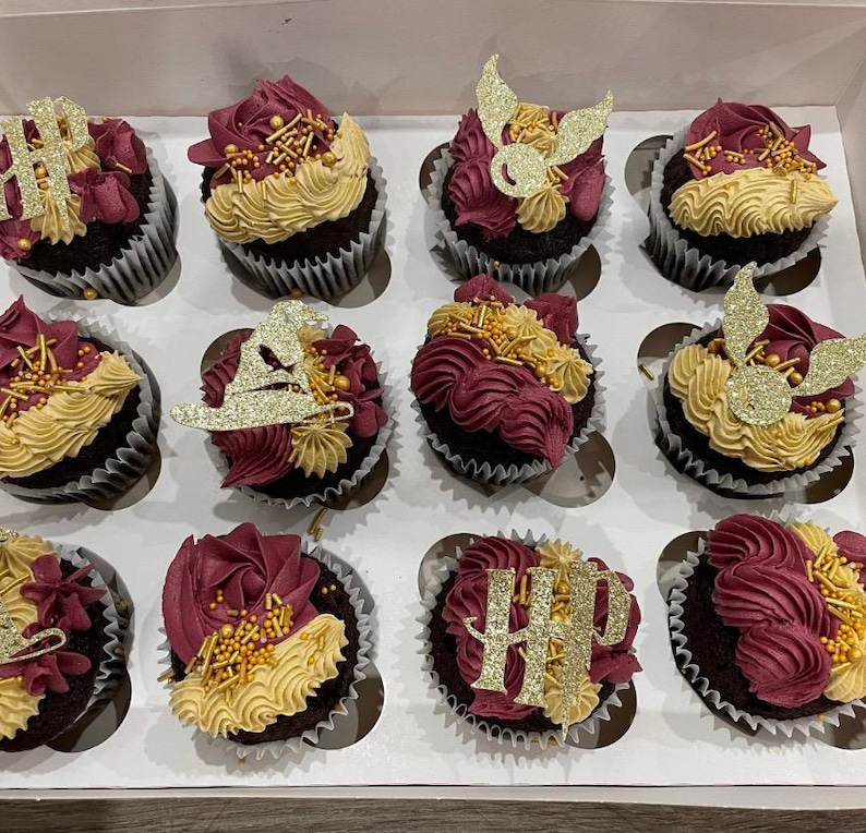 May include: A box of twelve chocolate cupcakes, each with burgundy and gold frosting. Some cupcakes are decorated with gold glitter, including the letters "HP", a sorting hat, and golden snitches.