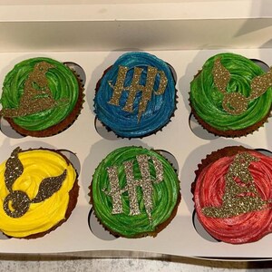 May include: Six cupcakes in a white box, each with colorful frosting and gold glitter decorations. The cupcakes have green, blue, yellow, and red frosting. The decorations include a wizard hat, lightning bolt, and golden snitch.