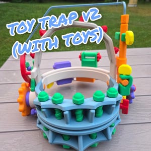 May include: A multi-colored plastic toy trap V2 with toys, featuring a light blue circular base with green bolt-like protrusions, a white arched frame, and an orange vertical post with yellow and green attachments, all constructed from various parts.