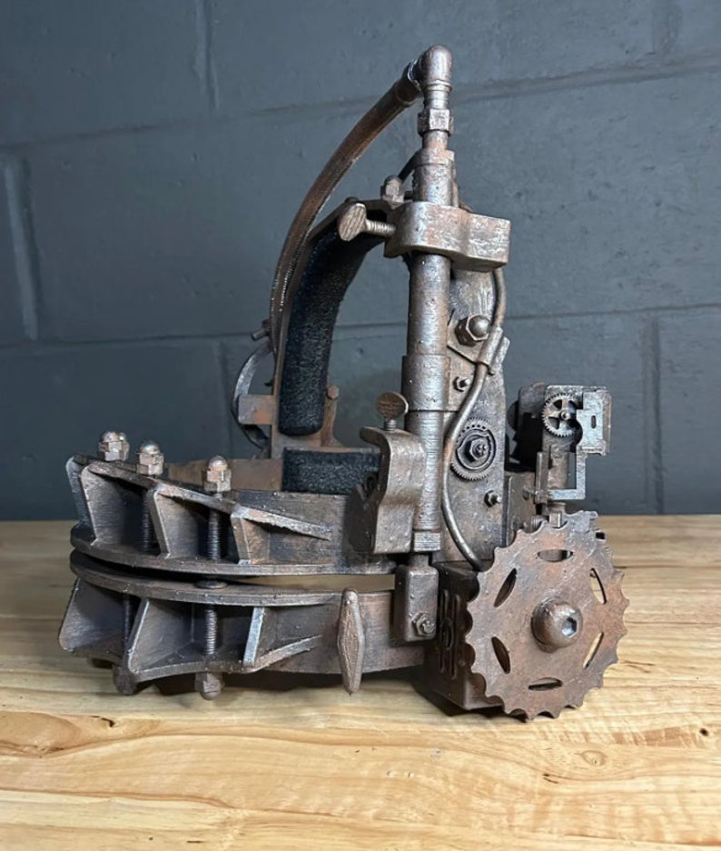 K&ouml;nnte beinhalten: Eine rostige Metall-Kopffalle mit einem Getriebesystem und einer schwarzen gepolsterten Kopfst&uuml;tze. Die Falle ist aus Metall und hat eine rostige Oberfl&auml;che. Die Falle ist so konzipiert, dass sie auf dem Kopf getragen werden kann und ein Getriebesystem hat, mit dem die Falle um den Kopf angezogen werden kann.