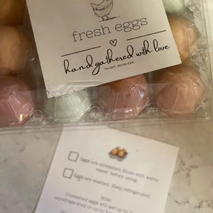 May include: A carton of fresh eggs with a white label that says "fresh eggs hand gathered with love" and a drawing of a chicken. The label also includes the text "The Last's 901-581-6306".