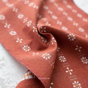 May include: Close-up of a terracotta-colored fabric with a repeating pattern of white and orange floral designs. The fabric is folded, revealing texture and detail. The word "FABLEISM" is printed on the fabric.