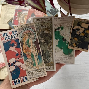 May include: A collection of vintage-style postcards featuring Art Nouveau illustrations and magazine covers. The postcards display text such as "The Pen Magazine" and "The House of the Trees". The color palette includes reds, blues, greens, and gold.