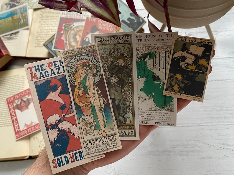 May include: A collection of vintage-style postcards featuring Art Nouveau illustrations and magazine covers. The postcards display text such as "The Pen Magazine" and "The House of the Trees". The color palette includes reds, blues, greens, and gold.