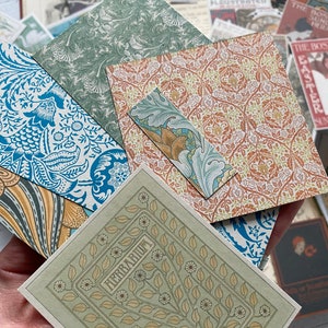 May include: A collection of patterned paper sheets in various sizes and designs. The papers feature floral and botanical motifs in shades of blue, green, orange, and beige. One sheet has the word "HERBARIUM" printed on it.
