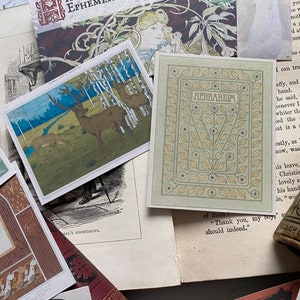 May include: A collection of vintage ephemera, including postcards and book pages. One postcard features deer in a forest scene, another reads "HERBARIUM" with floral accents. The items are arranged on a light-colored surface.