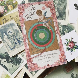 May include: A collection of vintage Valentine's Day cards and ephemera. The central card features an illustration of Cupid aiming at a target, with text that reads "Love's Target". Other cards include floral and romantic imagery.