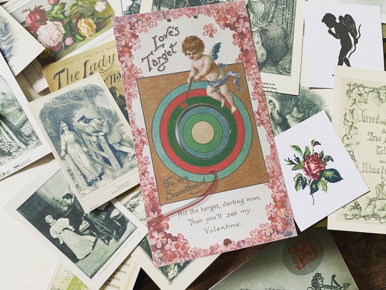 May include: A collection of vintage Valentine's Day cards and ephemera. The central card features an illustration of Cupid aiming at a target, with text that reads "Love's Target". Other cards include floral and romantic imagery.