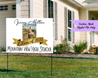 May include: A white graduation yard sign with the name "Jenny Hilton" and a photo of a young woman. The sign also includes "Class of 2022" on a gold banner and "Mountain View High School" in black text. The sign is on black metal stakes.