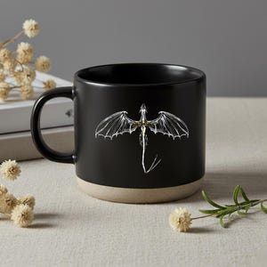 Op de afbeelding: Een set van drie keramische mokken met een gespikkelde, matte afwerking. De mokken zijn in crème, lichtgrijs en donkergrijs. Elke mok heeft een eenvoudig, minimalistisch ontwerp en een afgeronde handgreep. De mokken zijn op elkaar gestapeld.