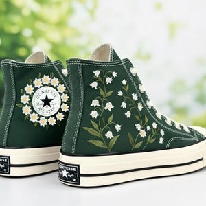Op de afbeelding: Donkergroene hoge sneakers met witte bloemenborduurwerk en een crèmekleurige zool. De sneakers hebben het Converse All Star-logo op de achterkant en een bloemenontwerp aan de zijkant. Een modieuze en unieke schoenoptie.