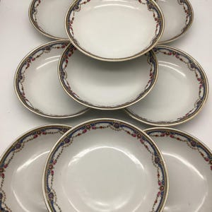 May include: Set of ten white porcelain soup bowls with a blue and gold rim and a floral design. The bowls are stacked in a pyramid shape.