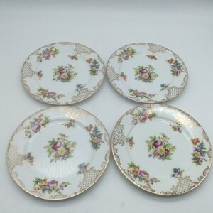 May include: Set of four white porcelain dessert plates with a gold rim and floral design. The plates feature a delicate floral pattern with pink, yellow, and blue flowers. The gold rim adds a touch of elegance to the design.