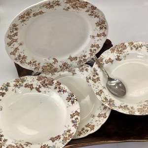 May include: A collection of antique white ceramic plates and serving dishes with a floral pattern in brown, blue, and yellow. Includes a large oval platter, several round plates, and a spoon.