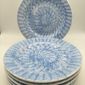 May include: A stack of six blue and white ceramic dinner plates with a speckled pattern. The plates have a slightly raised rim and a scalloped edge.
