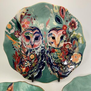 May include: A decorative ceramic plate with a scalloped edge and a gold rim. The plate features a teal background with a colorful floral design and two owls. The owls are depicted with vibrant colors and intricate details.