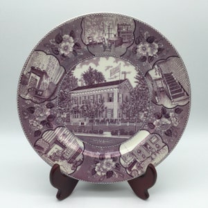 May include: A purple ceramic plate with a decorative design featuring a house, flowers, and various scenes. The plate reads "Lincoln's Home Springfield, Illinois".