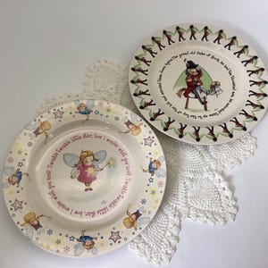 May include: Two decorative ceramic plates. One plate features a fairy with a wand and the text "Twinkle Twinkle little star". The other plate has a soldier on a horse with text around the rim. Both plates have a cream background.