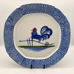 May include: A blue and white ceramic platter with a blue rooster design. The platter has a speckled blue glaze and a scalloped edge.