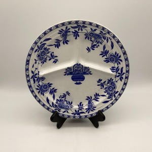 May include: A white divided plate with a blue floral design. The plate has three sections and a decorative border. The blue floral pattern includes flowers and leaves. The plate is on a black stand.