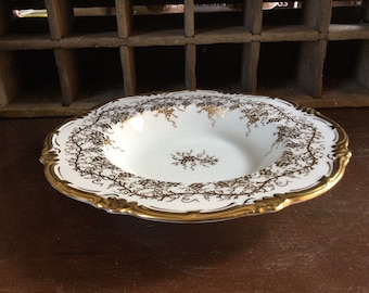 May include: A white porcelain bowl with a gold rim and intricate gold vine pattern. The bowl is perfect for serving soup, salad, or fruit.