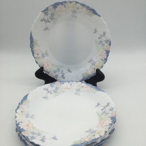 May include: A stack of five white ceramic dinner plates with a blue and floral design. The plates have a scalloped edge.