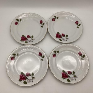 May include: Four white porcelain plates with a gold rim and a floral rose design. Each plate features a cluster of red roses with green leaves. The plates have a scalloped edge.