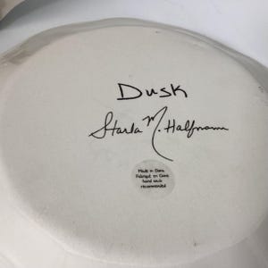 May include: A white ceramic plate with the word "Dusk" in black script, along with the signature "Starla M. Halfmann." A small sticker reads "Made in China, Fabriqu&eacute; en Chine, hand wash recommended."