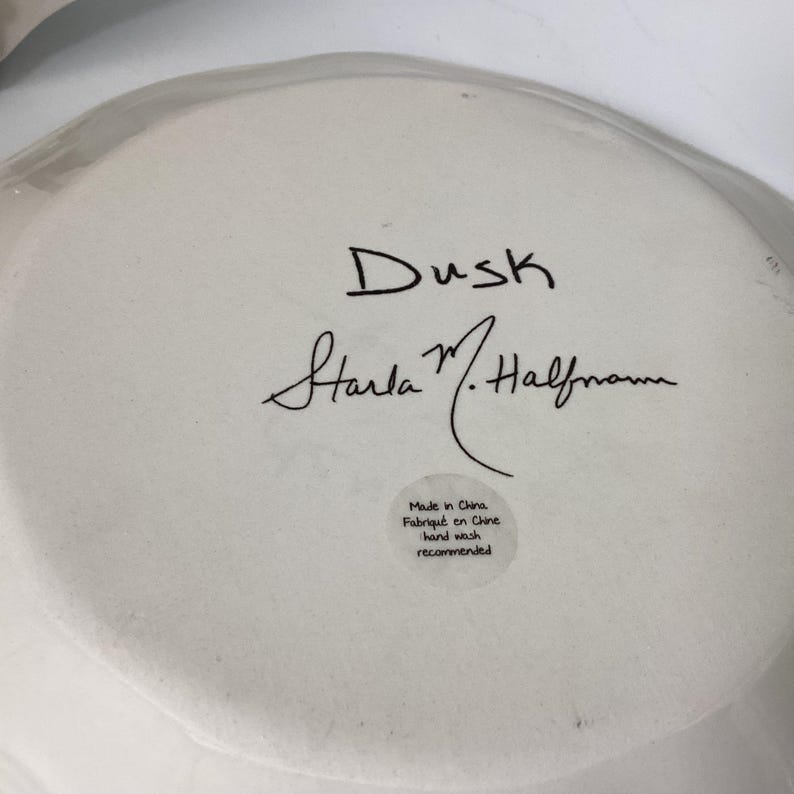 May include: A white ceramic plate with the word "Dusk" in black script, along with the signature "Starla M. Halfmann." A small sticker reads "Made in China, Fabriqu&eacute; en Chine, hand wash recommended."
