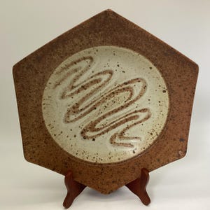May include: A hexagonal ceramic plate with a brown rim and a white center. The center has a swirling brown design.