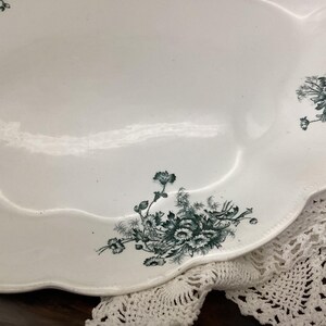 May include: White oval serving platter with a scalloped edge and dark green floral pattern. The vintage dish has a glossy finish and is partially resting on a white lace doily.