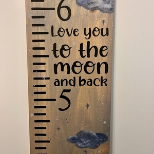 May include: A wooden growth chart with a gray stain and black markings. The chart features a whimsical design with clouds, stars, and the text "Love you to the moon and back". The numbers 6 and 5 are visible on the chart.