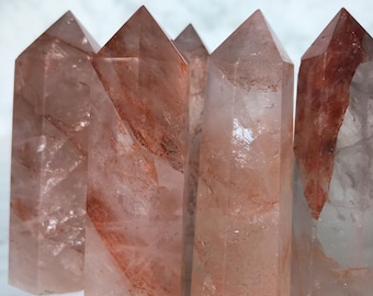 May include: A group of six clear quartz crystal points with red and orange inclusions. The points are arranged in a row, with the tips pointing upwards.