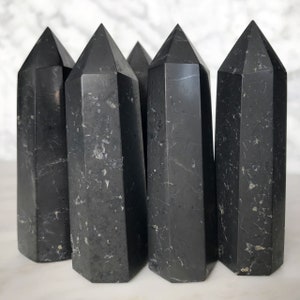 Peut inclure: Six pointes de cristal d'obsidienne noire, chacune avec un motif marbré naturel unique. Les pointes sont disposées en rangée, les pointes pointant vers le spectateur.