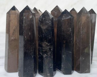 May include: A group of smoky quartz crystal points, also known as black quartz, arranged in a row. The points are various shades of brown and black, with some having a clear, glassy appearance.