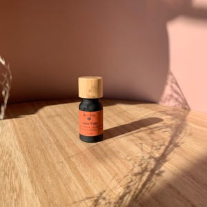 May include: A small, black glass bottle with a bamboo lid. The bottle contains Santa Trails essential oil blend with notes of orange, cinnamon, and clove. The label also says "Eco Love" and "10 ml".