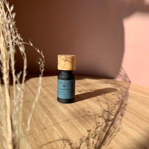 May include: A small black bottle with a wooden cap, labeled "Tea Tree" and "Eco Love" with a heart symbol. The bottle is sitting on a wooden surface.