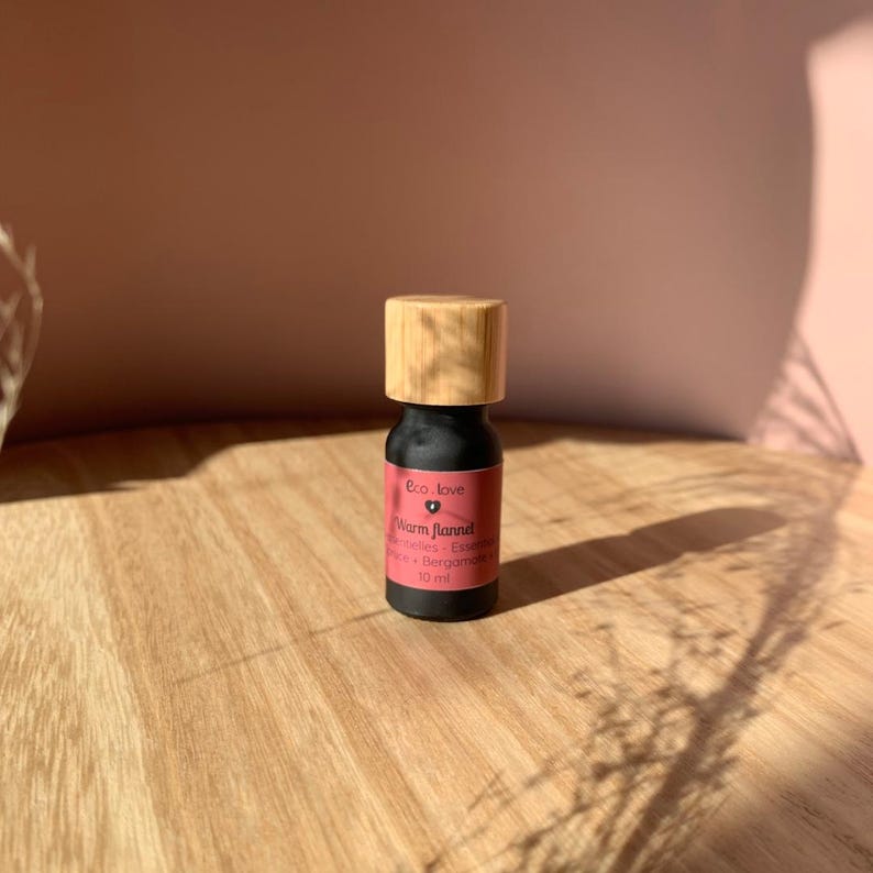 May include: A small black bottle with a bamboo lid, labeled "Warm Flannel" essential oil blend with pink and bergamot notes. The bottle is sitting on a wooden surface.